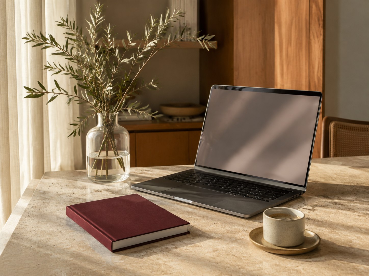 Una scrivania luminosa con un portatile, un quaderno bordeaux e una tazza di caffè
